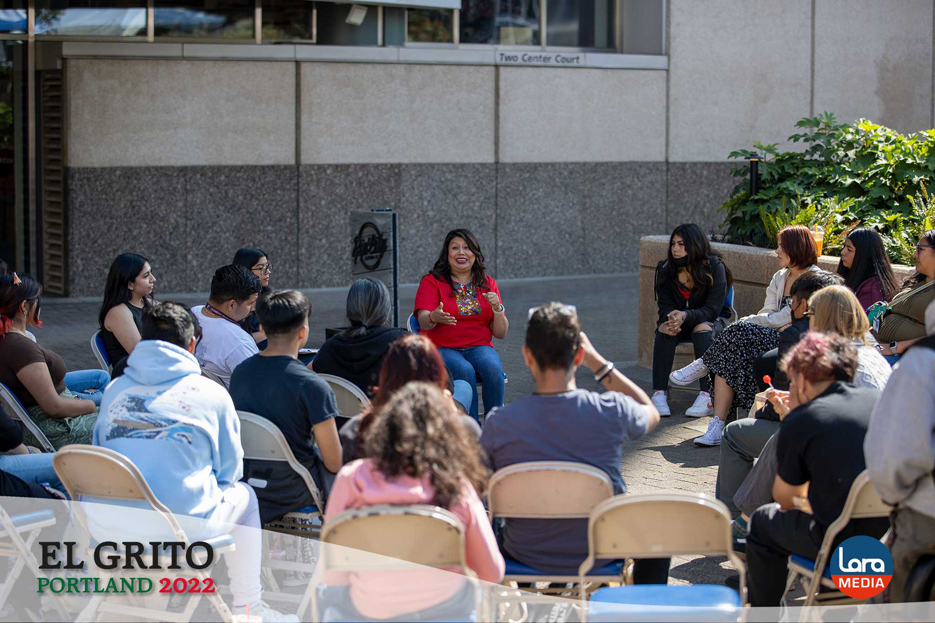Teresa Alonso-Leon, former Oregon State Representative, leads an outdoor discussion with a group of students seated in a circle at El Grito Portland. She gestures as she speaks, engaging the audience in a youth leadership and empowerment session.